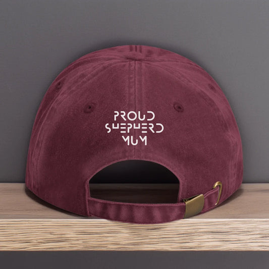 Vintage-style burgundy baseball cap with white embroidery that reads "Proud Shepherd Mum" in a bold modern font. Designed as a personalised gift for German Shepherd dog mums and proud dog parents.