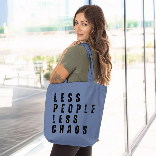 Woman holding a blue tote bag that reads "LESS PEOPLE LESS CHAOS" on the front — a bold, minimalist design for dog parents, rescue advocates, and introverts who prefer the calm company of dogs over people. The back of the bag reads "that's why I adopt dogs."


