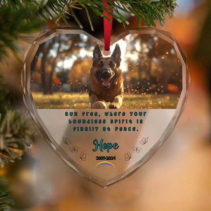 Heart-shaped memorial ornament hanging on a Christmas tree, featuring a photo of a happy dog running through autumn leaves. Below, a personalised tribute reads “Run free, where your boundless spirit is finally at peace,” with the name “Hope” and the dates “2009–2024.”