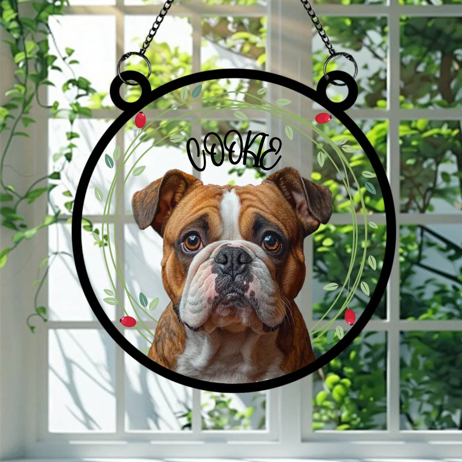A round glass suncatcher featuring a realistic portrait of a brown and white bulldog named Cookie, surrounded by a delicate green leaf and berry wreath. This personalised decoration is a heartfelt keepsake for dog lovers, perfect for hanging in a sunny window.