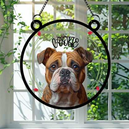 A round glass suncatcher featuring a realistic portrait of a brown and white bulldog named Cookie, surrounded by a delicate green leaf and berry wreath. This personalised decoration is a heartfelt keepsake for dog lovers, perfect for hanging in a sunny window.